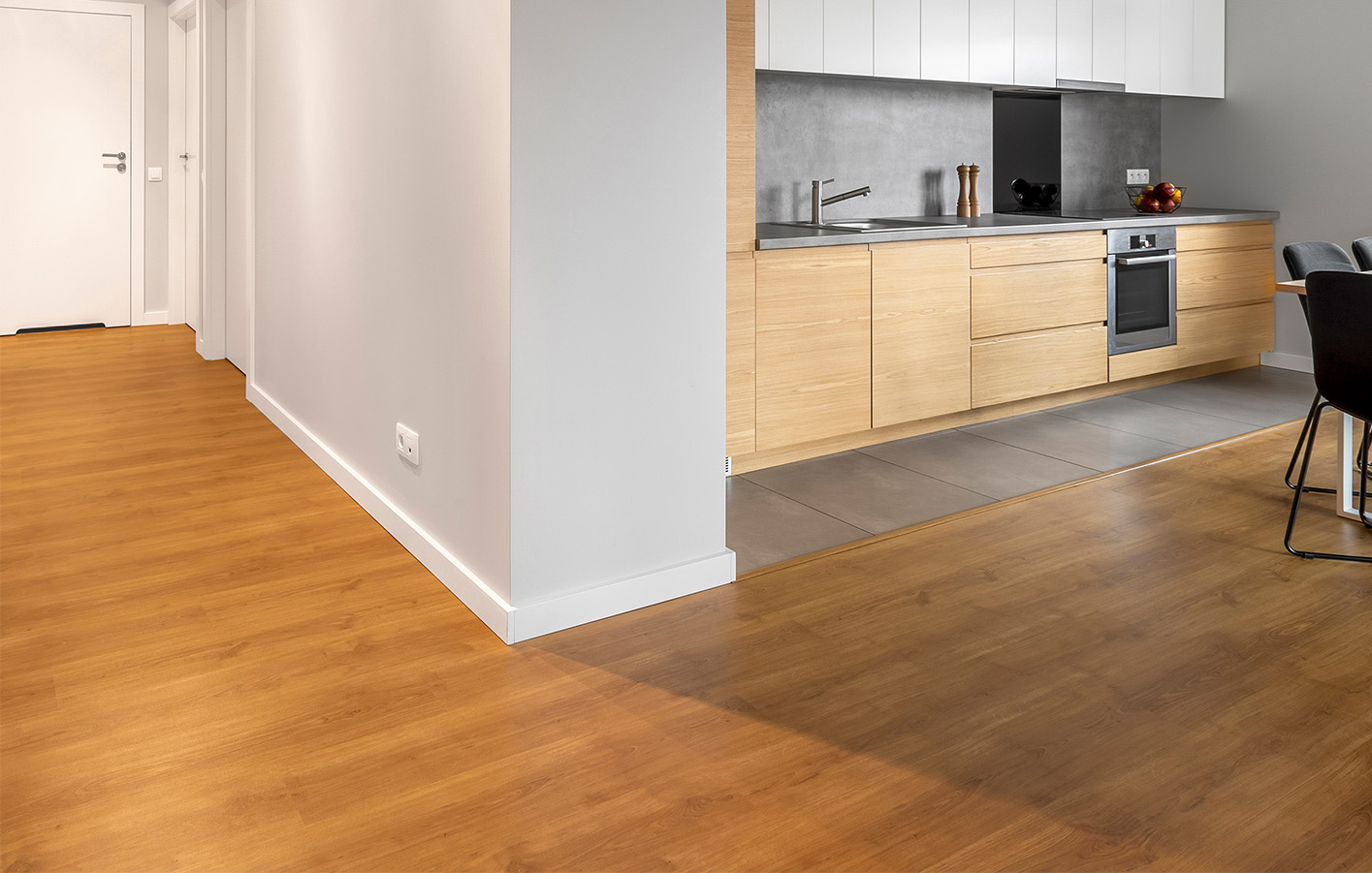 Moderne Küche mit weißer Sockelleiste und Holzoptikboden Moderne Küche mit weißer Sockelleiste, Holzoptikboden und grauen Fliesen im Bodenbereich.